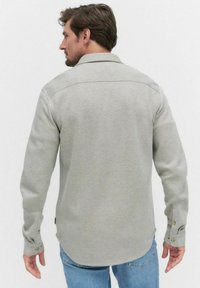 Graues Langarmhemd mit strukturiertem Kragen und knöpfbaren Manschetten; aus einem strukturierten Stoff mit leicht abgerundetem Saum.