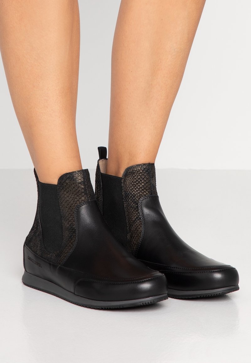 Botas negras de tobillo con punta de cuero liso, lados texturizados con patrón de reptil, paneles elásticos y una pestaña en el talón.