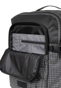 Zaino a scacchi bianco e nero con un cappuccio zip nero, dotato di scomparti interni grigi e un logo del marchio in evidenza. Tessuto testurizzato.