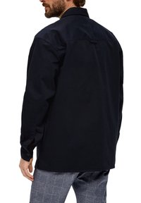 Giacca in cotone blu navy con colletto aperto, maniche lunghe e polsini con bottone. Presenta uno yoke posteriore e un orlo dritto.