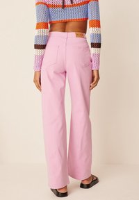 Rosa denimbyxor med vida ben, hög midja, bakfickor och subtila sömnadsdetaljer. Kombinerade med en färgglad stickad topp.