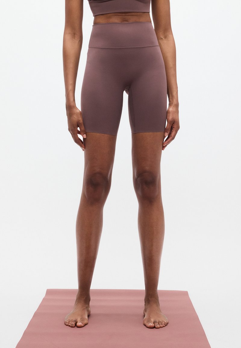 Μωβ ποδηλατικά σορτς με ψηλή μέση, κατασκευασμένα από λεία, ελαστική ύφανση. Διαθέτουν εφαρμοστή κοπή με μήκος έως το γόνατο και ελάχιστη ραφή.