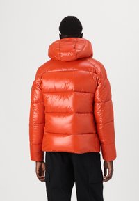 Puffer jacket in shiny orange material, featuring a hood, quilted pattern, and elastic cuffs. Displayed from the back with a relaxed fit.