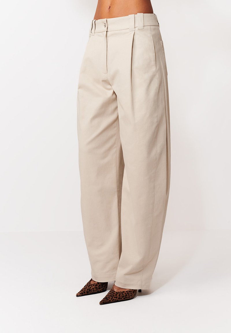 Béžové široké nohavice s vysokým pásom v kombinácii so špicatými lodičkami s leopardím vzorom na bielom pozadí.