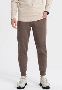 Brune tapered joggerbukser lavet af blødt stof, med sidelommer og ribbede manchetter, parret med lyse sneakers.