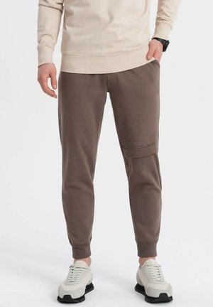 Pantaloni jogger a forma affusolata marroni, realizzati in un morbido tessuto, con tasche laterali e polsini a coste, abbinati a sneakers chiare.