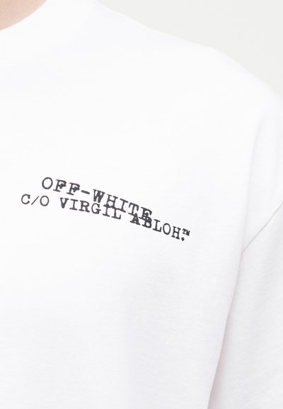 Λευκό πουκάμισο με μαύρο κείμενο «OFF-WHITE c/o VIRGIL ABLOH™» τυπωμένο διαγώνια στο πάνω μέρος του στήθους.