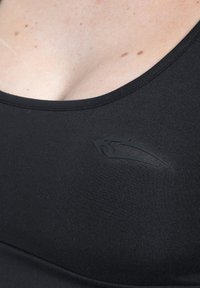 Zwart sportbeha gemaakt van rekbare stof. Heeft een diepe ronde halslijn en een klein zwart logo aan de linkerkant. Soepele textuur.