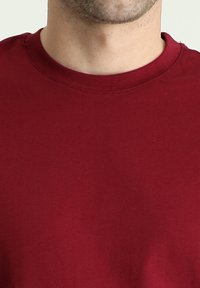 Burgundowa koszulka z okrągłym dekoltem, wykonana z gładkiego bawełnianego materiału. Posiada prosty, nieskomplikowany design bez widocznych wzorów lub akcentów.