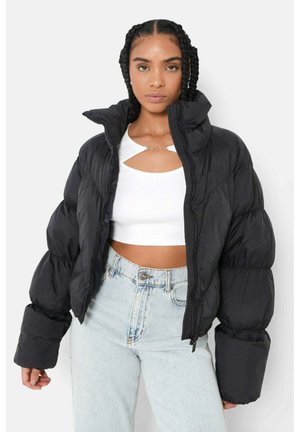 Zwarte pufferjack met een hoge kraag en ritsluiting, met volumineuze, doorgestikte mouwen. Gecombineerd met een witte cropped top en lichte denim jeans.