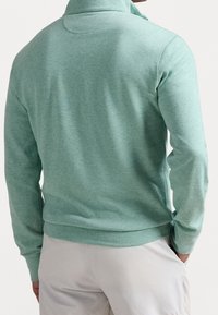 Pullover verde a maniche lunghe realizzato in tessuto morbido con colletto alto e polsini a coste. Tessuto liscio con cuciture minime e silhouette aderente.