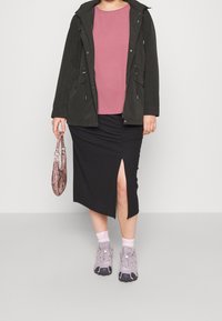 Svart ribbad kjol med en sida slits, rosa topp och mörkgrön jacka. Grå sneakers med svarta sålar och en mönstrad väska.