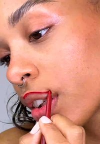Red lip liner is being applied to the lips. The hand holding the liner has light polish. Skin has a smooth texture and a natural tone.