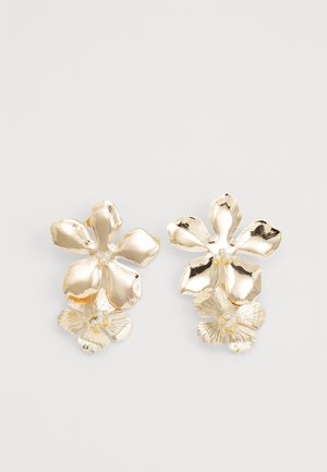 Pendientes florales en tono dorado con pétalos texturizados y pequeños acentos de perlas. Presentan dos formas de flor distintas; diseño ligero adecuado para llevar.