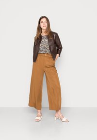 Jaqueta curta de couro castanho, blusa estampada de flores, calças largas castanhas e sandálias brancas de salto bloco. Texturas suaves e ajuste personalizado.