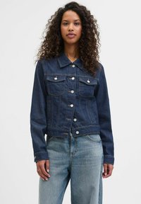 Tamsiai mėlynas džinsinis švarkas su apykakle, mygtukų užsegimu ir dviem krūtinės kišenėmis. Yra sutrumpintas modelis ir ilgomis rankovėmis.