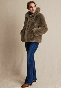 Faux fur-jacka i olivgrönt med en bred krage, framknappar och sidofickor, tillsammans med mörkblå vida jeans och bruna stövlar.
