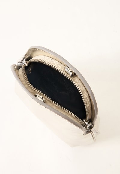 Petite pochette en cuir beige avec fermeture éclair argentée partiellement ouverte montrant une doublure intérieure noire sur fond blanc.
