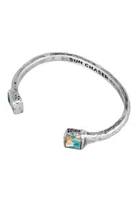 Silverfärgad manschettarmband med en strukturerad yta, prydd med två rektangulära accentstenar i turkos och orange. Inskrift: "SUN CHASER."