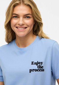 Ljust blå bomull t-shirt med kort ärm som har texten "Njut av processen" i fet svart font på framsidan. Slät textur.