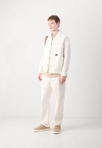 White denim jacket with front pockets, beige striped shirt underneath, white pants, and beige sneakers. Simple, clean design with minimal accents.
