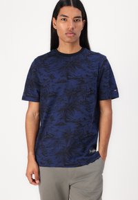 Tricou bleumarin cu un model de palmieri în negru. Guler rotund, mâneci scurte, cu un mic patch de logo la tiv. Material din amestec de bumbac.