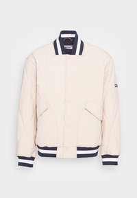 Vaaleanbeige tikattu bomber-takki, jossa on tummansiniset ribbireunat hihansuissa ja kauluksessa. Takissa on nappisuljenta ja kaksi etutaskua.