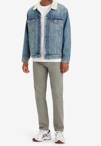 Jasnoniebieska kurtka dżinsowa z białym kołnierzem z polaru, zestawiona z białą koszulką i szarymi spodniami. Białe trampki z czerwonymi i czarnymi akcentami.