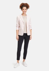 Růžový blazer v odstínu nude, lehký materiál, přiléhavý střih, s klopami, dvěma předními kapsami. Nositý přes béžový svetr a kombinovaný s černými kalhotami a bílými teniskami.