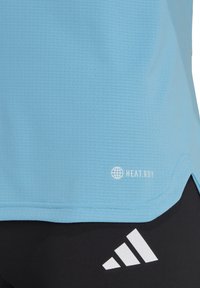 Lichtblauw sportshirt met een gestructureerd oppervlak, voorzien van het "HEAT.RDY" logo in het wit en een geprofileerde zoom, gecombineerd met zwarte shorts en een wit Adidas-logo.