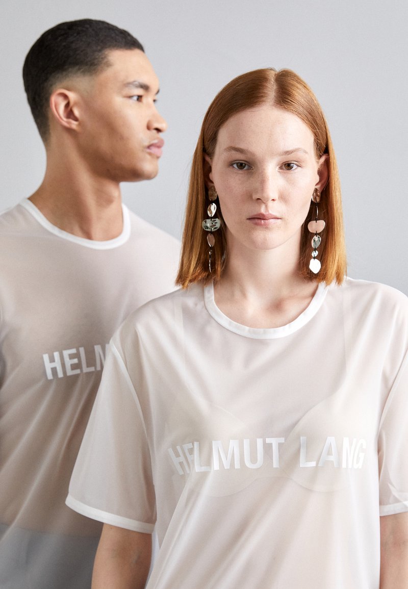 Transparente weiße T-Shirts mit "HELMUT LANG" in fetten weißen Buchstaben bedruckt, getragen von zwei Models. Eines hat lange rote Haare, das andere kurze dunkle Haare.