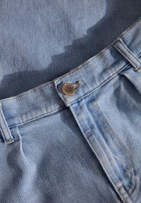Lichtblauwe denimstof met een zichtbare metalen knoop bij de tailleband, met een gladde textuur en een klassiek vijf-pocket ontwerp.