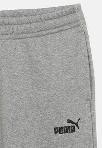 Sivé teplákové nohavice s jemnou textúrou, elastickým pásom a čiernym vyšívaným logom Puma na ľavom stehne.