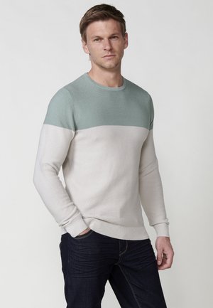 Pull en tricot léger avec une texture côtelée. La moitié supérieure est teal et la moitié inférieure est beige, avec un col rond et des poignets ajustés.