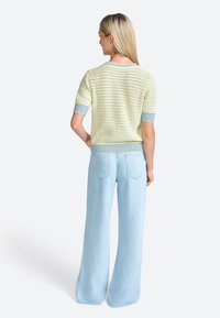 Knitted short-sleeve sweater in soft yellow with blue stripes at the cuffs and bottom, paired with light blue wide-leg jeans.