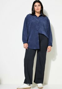 Marineblauwe corduroy oversized shirt met twee borstzakken, gecombineerd met zwarte broek met streep en witte sneakers.