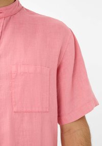 Camicia a maniche corte in tessuto rosa chiaro, con colletto rialzato, taschino a toppa sul lato sinistro del petto e una vestibilità comoda con cuciture a vista.