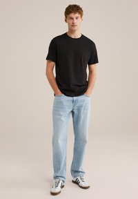 Camiseta de algodón negra, con un corte relajado, combinada con jeans de denim azul claro. Los zapatos son blancos con acentos negros, con un diseño clásico.