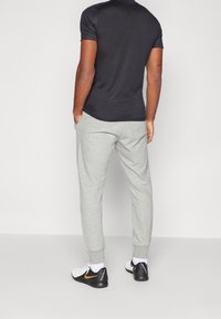 Schwarzes T-Shirt mit kurzen Ärmeln und hellgraue Sweatpants, die eine lässige Passform bieten. Die Schuhe sind weiß mit schwarzen und goldenen Akzenten.