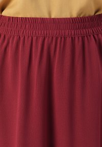 Jupe bordeaux avec une surface texturée et une taille élastique. Le tissu tombe doucement, présentant un design lisse et fluide.