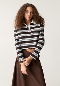 Hnedo-biely pruhovaný cropped polo s dlhým rukávom a svetlomodrým golierom, ktorý má voľný strih a mäkkú textúru.