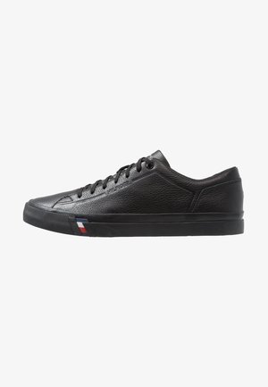 Sneaker in pelle nera con superficie testurizzata, punta arrotondata, suola piatta e lacci neri. Presenta un accento colorato vicino alla suola.