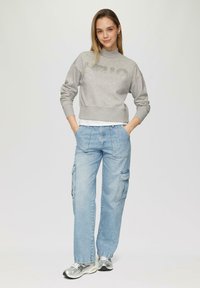 Grijze cropped sweatshirt met de tekst "HELLO", gecombineerd met lichtblauwe cargobroek met zakken. Model draagt zilveren sneakers.