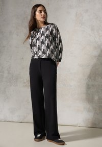 Lange zwarte broek gecombineerd met een grijze geborte blouse met een houndstooth ontwerp. De stof lijkt glad met een ontspannen pasvorm.