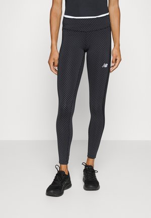 Leggings noirs avec un motif à pois, taille haute et panneaux latéraux. Portés avec des chaussures de sport noires, mettant en valeur un design épuré.