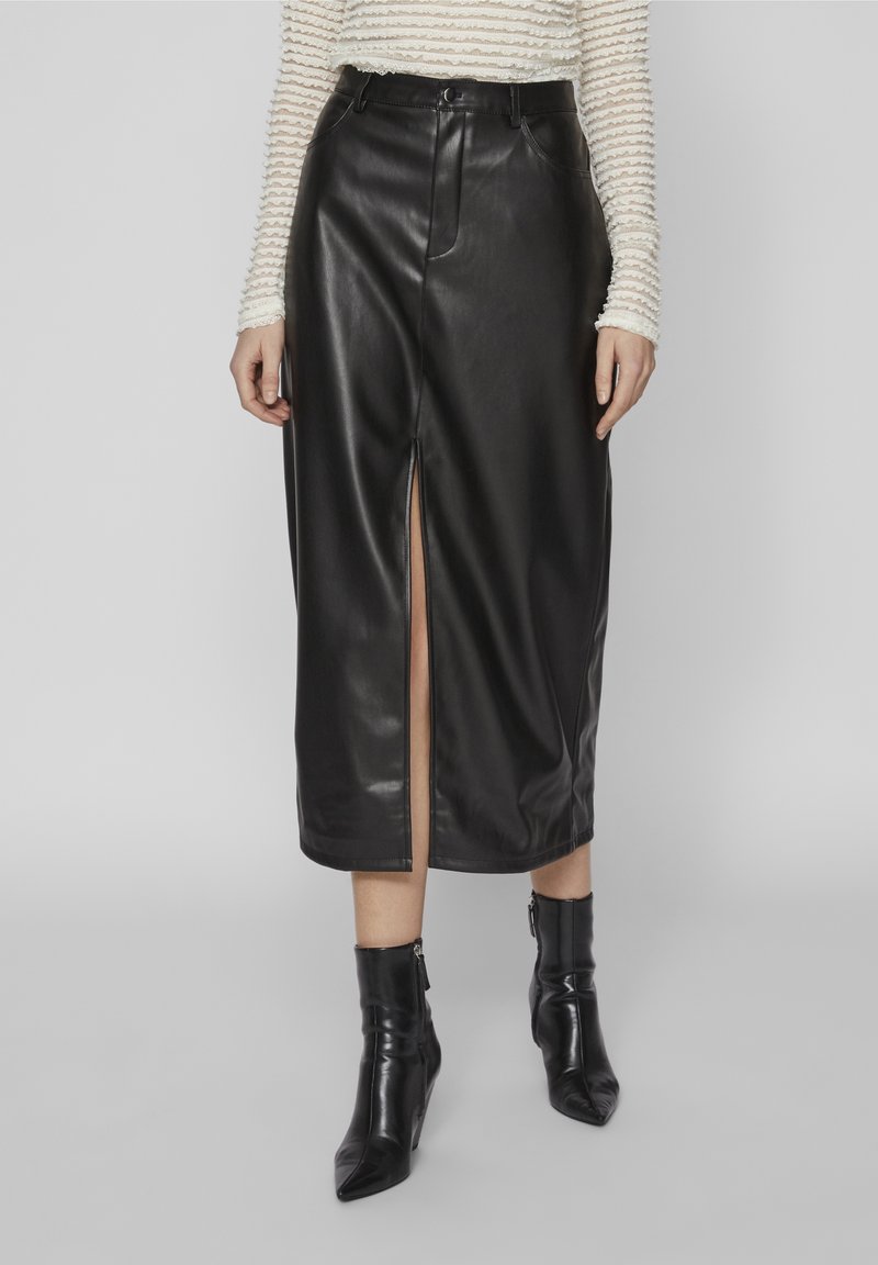 Jupe midi en similicuir noir avec fente à l'avant, portée avec un haut ajusté à manches longues texturé et des bottines noires à bout pointu.