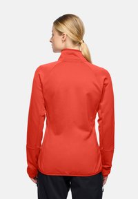 Maglietta atletica rossa a maniche lunghe con colletto alto e tessuto texturizzato. Presenta maniche raglan e una silhouette aderente.