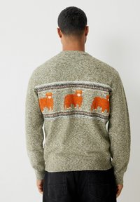 Zelený pletený sveter s pruhovanou páskou a oranžovými siluetami kráv, horizontálnymi pruhmi a rífovaním na spodnom leme a manžetách.