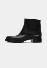 Botas de tornozelo em borracha preta com acabamento liso, bico arredondado, design minimalista e sola texturada grossa; apresenta a marca "VALENTINO".