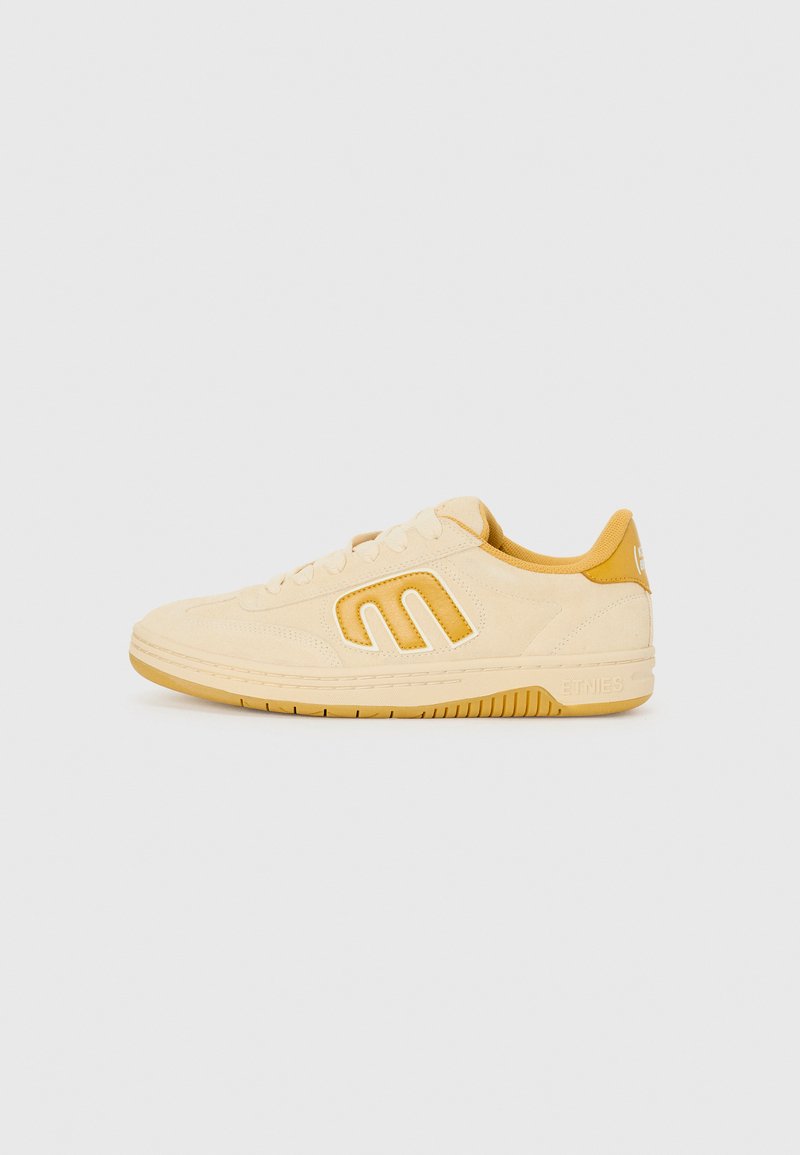 Beige semišové tenisky se žlutými akcenty, jednoduchý design, plochá gumová podrážka a branding na patě.